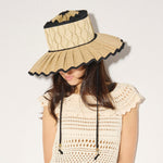 Woman wearing a beige sun hat with black trim on a plain background