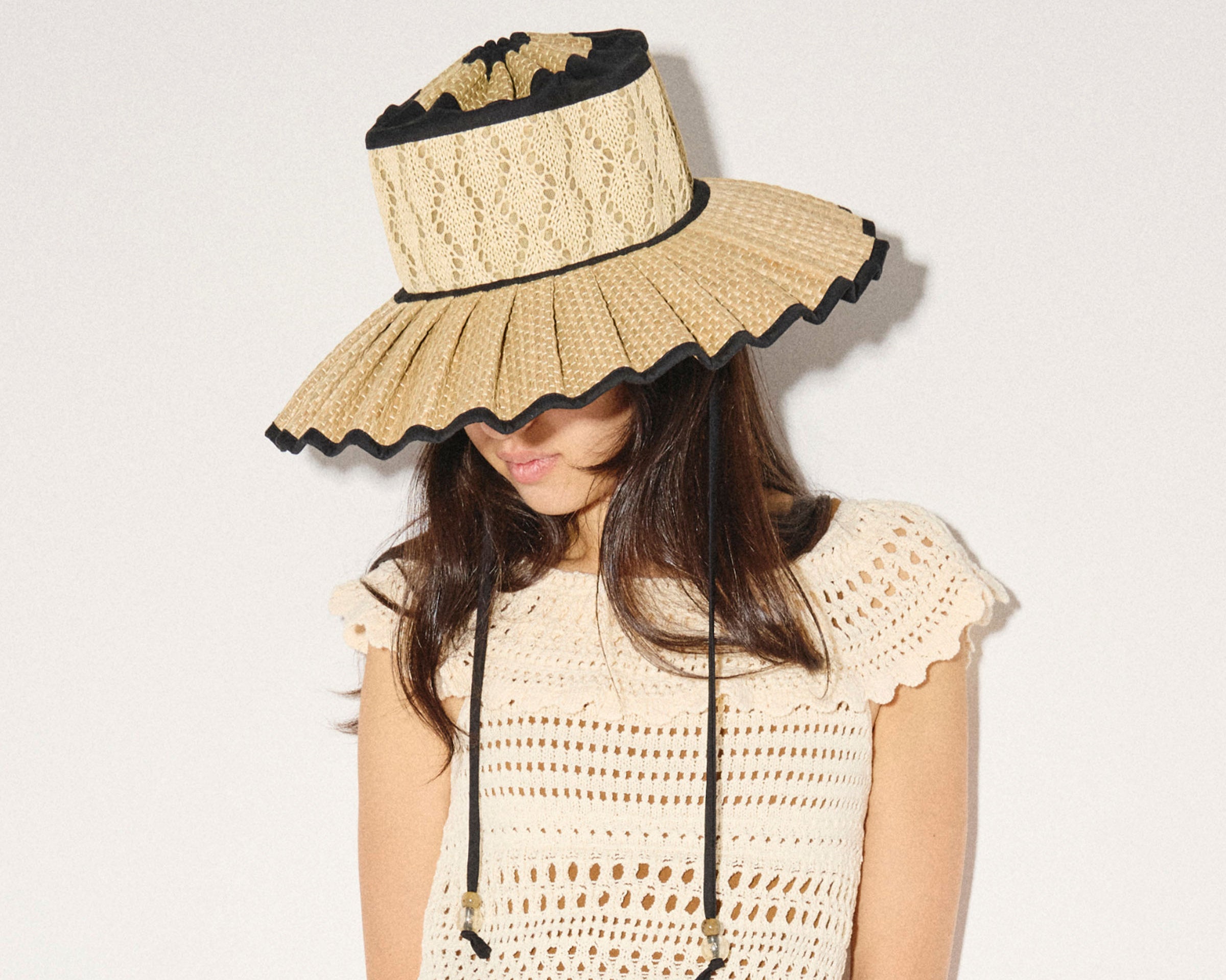 Woman wearing a beige sun hat with black trim on a plain background
