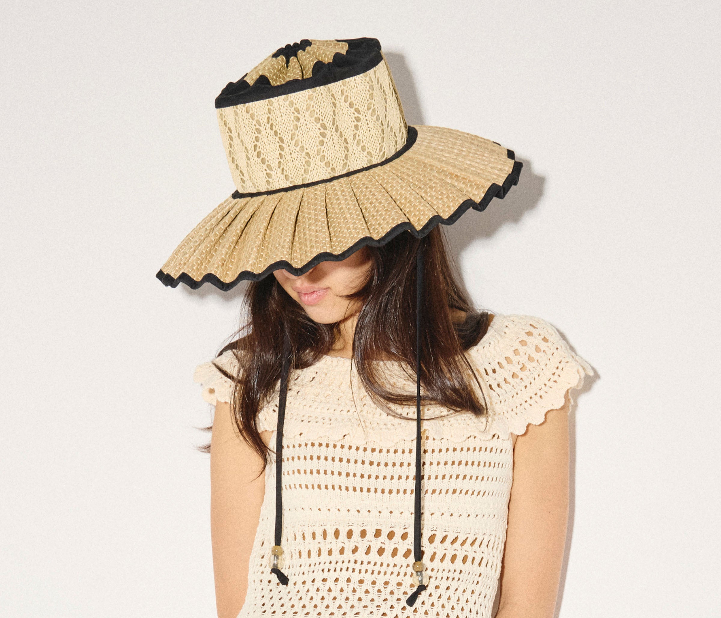 Woman wearing a beige sun hat with black trim on a plain background