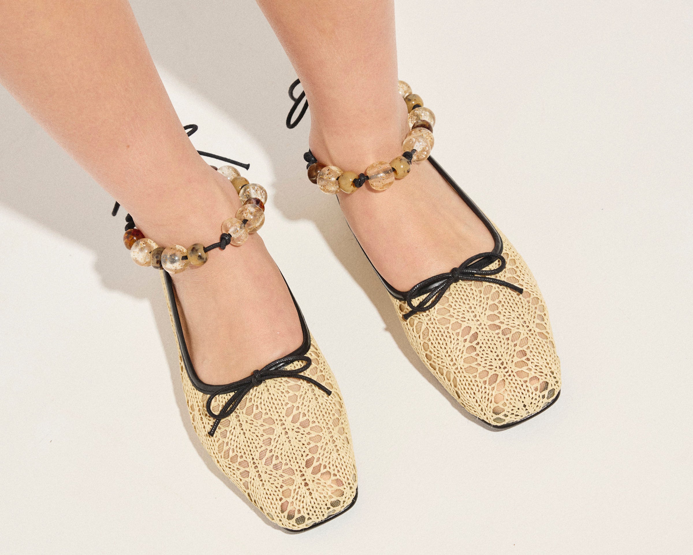Beige lace-up shoes worn with decorative anklets on a light background