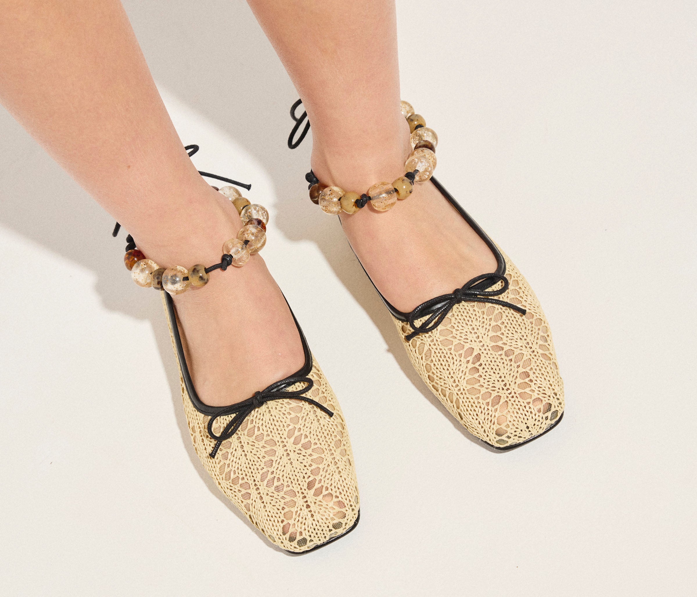 Beige lace-up shoes worn with decorative anklets on a light background