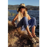 Person sitting by a lake wearing the Lorna Murray x Freda Salvador wide-brimmed hat and flats.