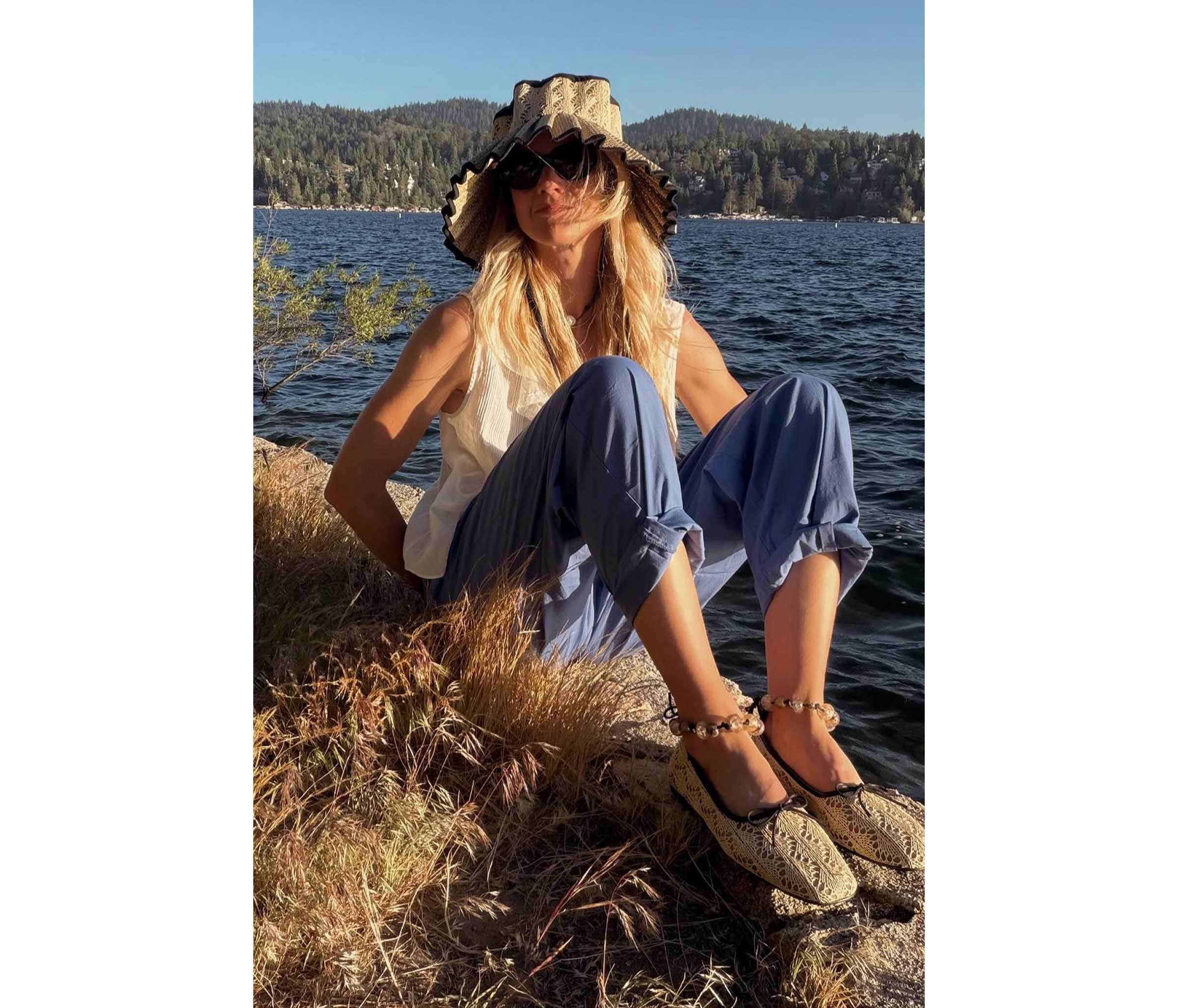 Person sitting by a lake wearing the Lorna Murray x Freda Salvador wide-brimmed hat and flats.