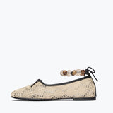 Beige flat shoe with lace design and wooden beads on a white background