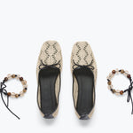 Pair of beige lace shoes with black soles on a white background, accompanied by two matching bracelets.