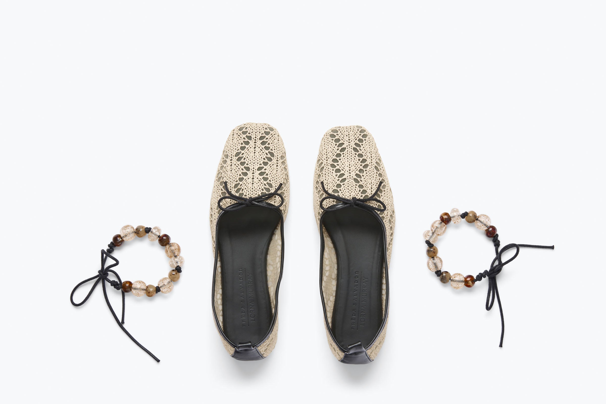 Pair of beige lace shoes with black soles on a white background, accompanied by two matching bracelets.